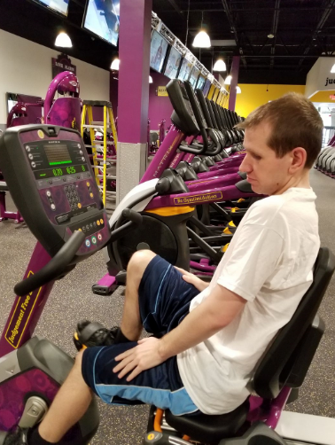 Kyle sitting on a stationary bike at a gym.