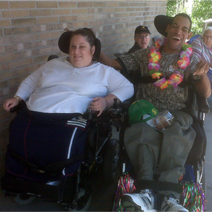 A woman and man sitting next to each other in wheelchairs. The man has his arm around the woman and he is smiling.