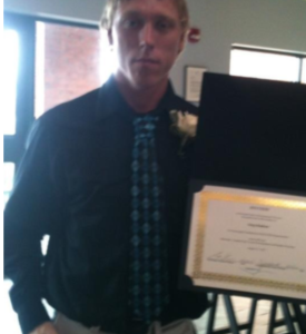 Man in dress clothes standing and holding a certificate.