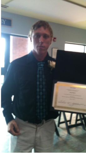 Man in dress clothes standing and holding a certificate.