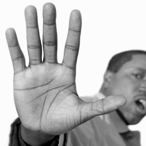 Black and white photo of African-American man holding his hand up toward the camera. His face is blurred and his mouth is staying, "Stop." White background. Copyspace. Chessielypse image. (Model release for Chessielypse approved by administration.