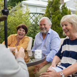 Senior friends sitting in the garden on a summers day together. They are sitting and having a laugh over a cup of tea.